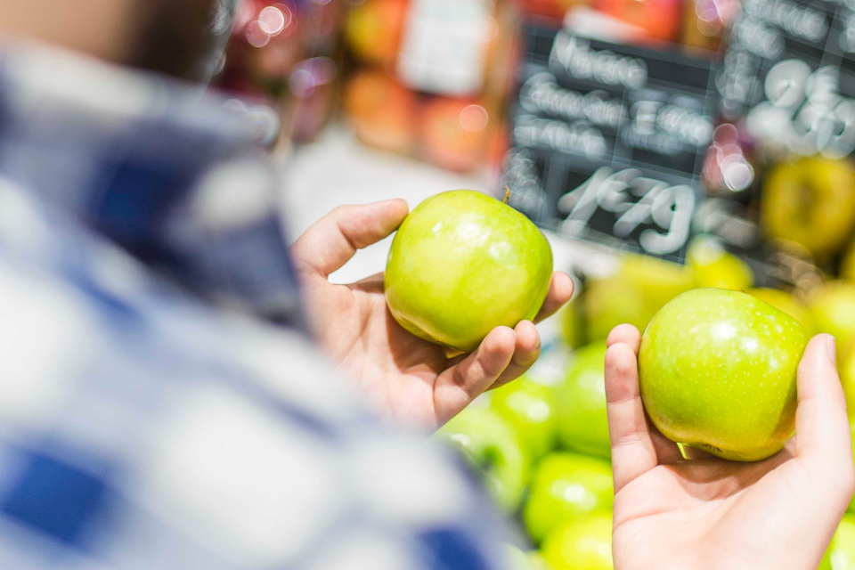 Dans un supermarché, un consommateur hésite entre deux produits (pommes) pour consommer plus responsable et plus sain.